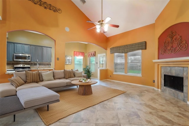 living area featuring light tile patterned floors, baseboards, high vaulted ceiling, a fireplace, and ceiling fan