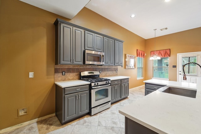 kitchen featuring gray cabinetry, a sink, backsplash, appliances with stainless steel finishes, and light countertops