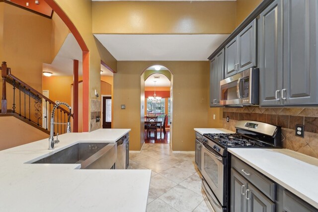 kitchen with arched walkways, a sink, light countertops, appliances with stainless steel finishes, and backsplash