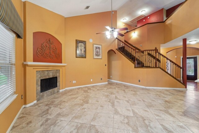 unfurnished living room with visible vents, baseboards, a tiled fireplace, arched walkways, and high vaulted ceiling