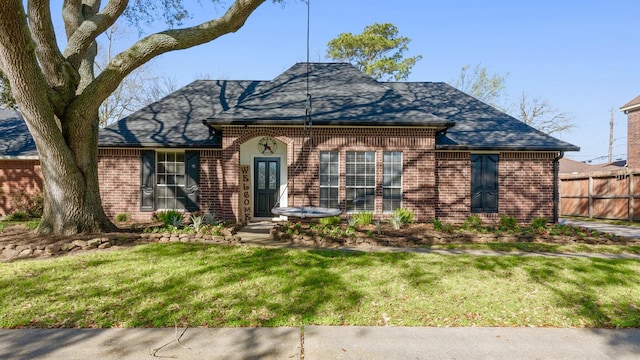 view of front of property featuring brick siding, roof with shingles, a front lawn, and fence