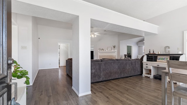 interior space with a ceiling fan, dark wood-style floors, baseboards, lofted ceiling, and a fireplace