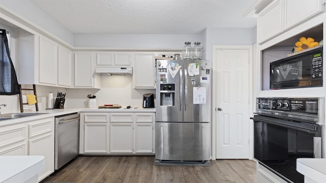 kitchen with a sink, black appliances, wood finished floors, and under cabinet range hood