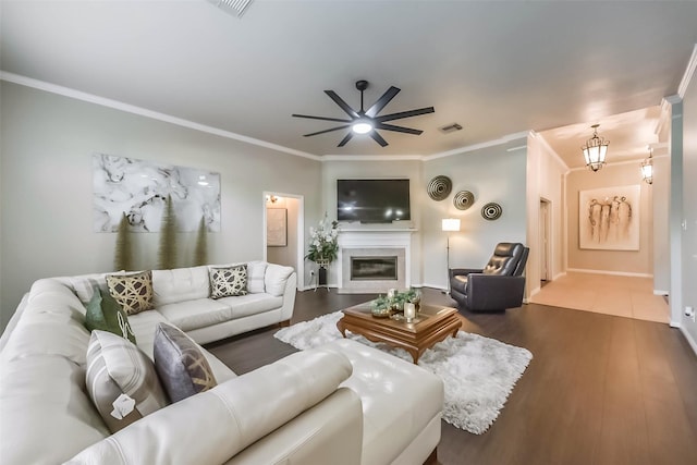 living area with a glass covered fireplace, crown molding, visible vents, and dark wood-style flooring