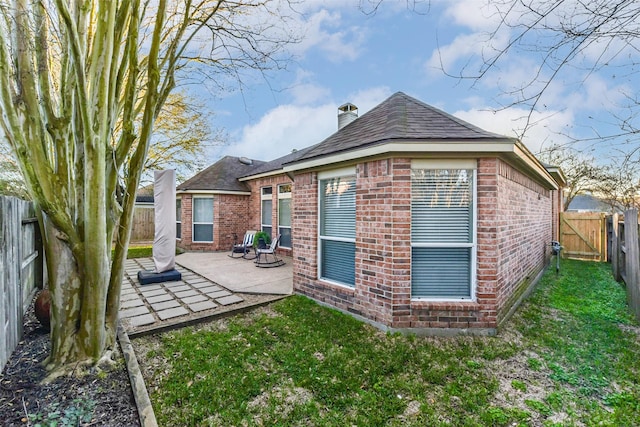 back of property featuring brick siding, a fenced backyard, a chimney, and a patio