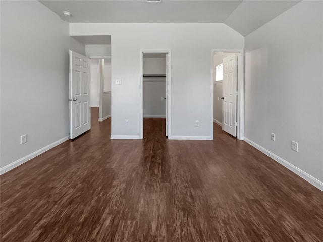 unfurnished bedroom featuring a walk in closet, baseboards, dark wood-type flooring, and vaulted ceiling