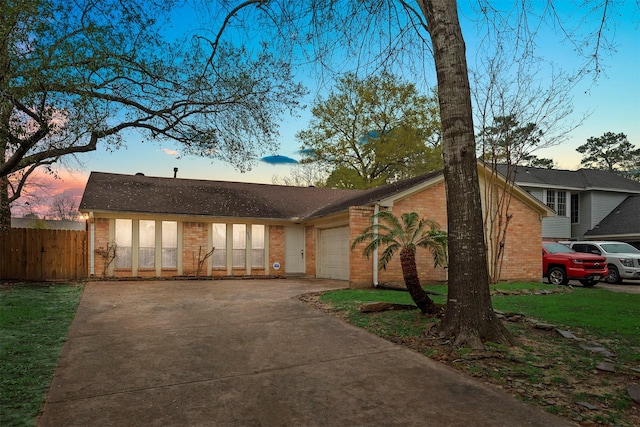 view of front of home with brick siding, an attached garage, concrete driveway, and fence