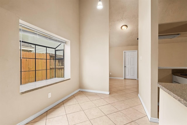 spare room featuring light tile patterned floors, a textured ceiling, and baseboards