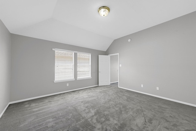 carpeted empty room featuring baseboards and vaulted ceiling