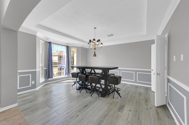 dining room featuring a tray ceiling, a decorative wall, light wood-style floors, and visible vents