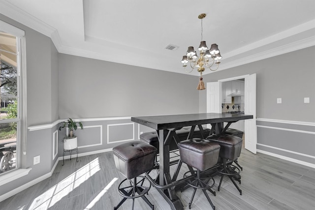 dining space with a tray ceiling, a notable chandelier, wood finished floors, and visible vents