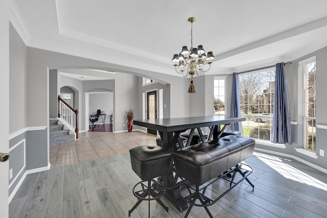 dining area with a raised ceiling, stairway, wood finished floors, and arched walkways