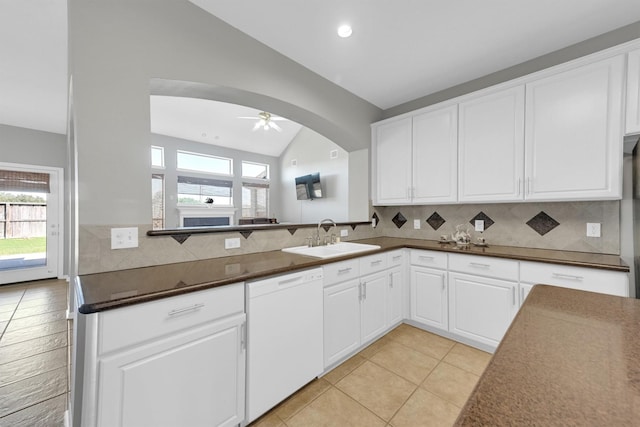 kitchen with a sink, dark countertops, tasteful backsplash, arched walkways, and white dishwasher