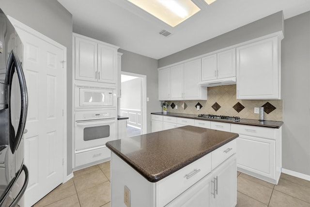 kitchen with white appliances, light tile patterned floors, backsplash, and a center island