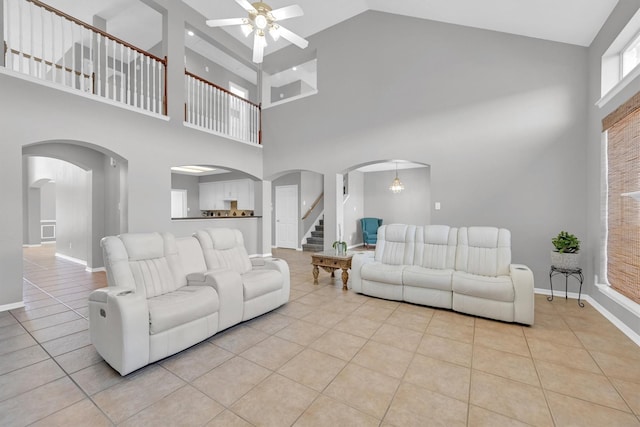 living room featuring light tile patterned flooring, arched walkways, a ceiling fan, and baseboards