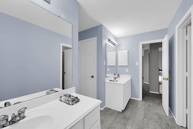 bathroom featuring two vanities, baseboards, and a sink