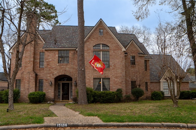 view of front of home with brick siding, roof with shingles, and a front lawn