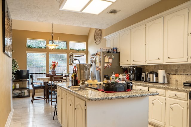 kitchen featuring visible vents, freestanding refrigerator, decorative backsplash, white cabinets, and a center island