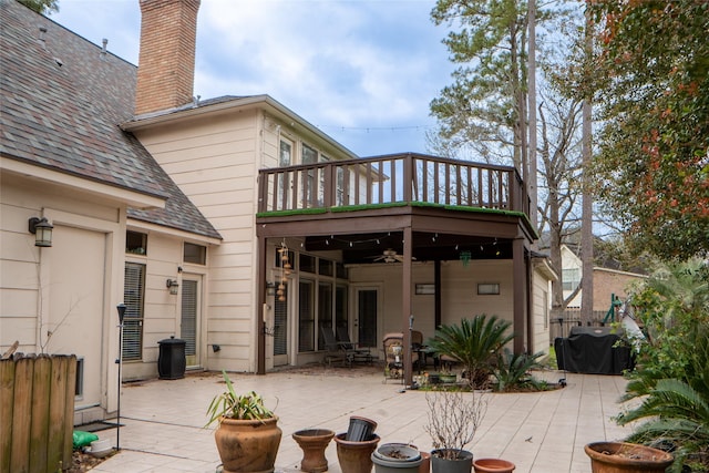 back of house with fence, roof with shingles, a chimney, a balcony, and a patio area