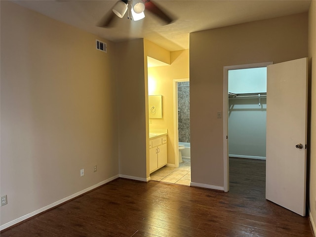 unfurnished bedroom featuring visible vents, a walk in closet, ensuite bathroom, wood finished floors, and a closet