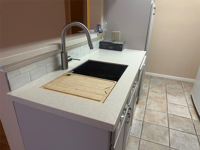 kitchen with baseboards, light tile patterned flooring, a sink, light countertops, and backsplash