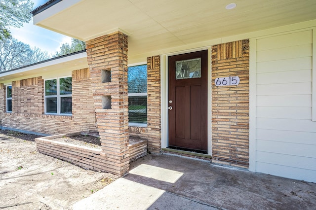 view of exterior entry featuring covered porch and brick siding