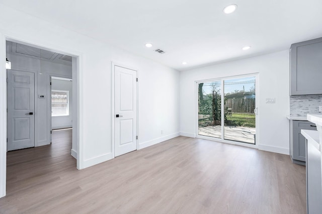 unfurnished living room featuring light wood finished floors, visible vents, baseboards, attic access, and recessed lighting