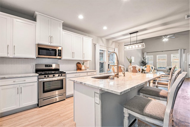 kitchen with light stone countertops, a breakfast bar area, appliances with stainless steel finishes, white cabinetry, and a sink