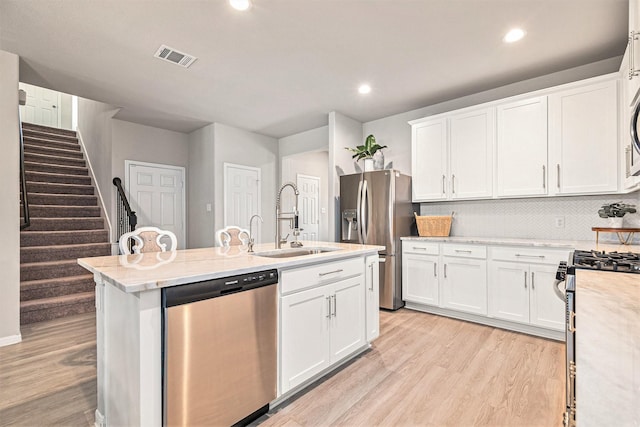 kitchen with a center island with sink, a sink, white cabinets, appliances with stainless steel finishes, and light wood-type flooring