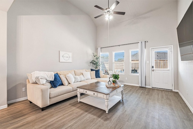 living area featuring a ceiling fan, wood finished floors, baseboards, and high vaulted ceiling