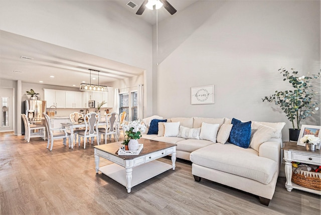 living area featuring a towering ceiling, visible vents, light wood-style flooring, and a ceiling fan