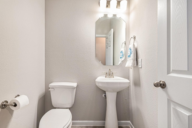 bathroom with baseboards, toilet, and a textured wall