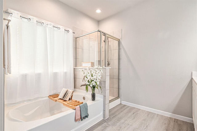 bathroom with a stall shower, baseboards, wood finished floors, and a bath