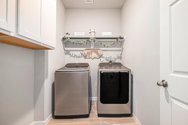 laundry area featuring visible vents, baseboards, washing machine and clothes dryer, light wood-style flooring, and cabinet space