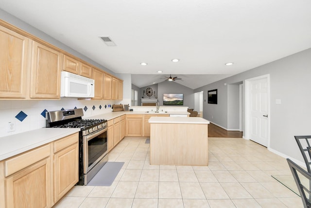 kitchen featuring light tile patterned floors, white microwave, visible vents, light brown cabinets, and stainless steel range with gas stovetop