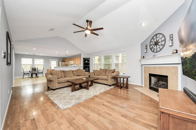 living area with a tiled fireplace, a healthy amount of sunlight, light wood-style floors, and ceiling fan