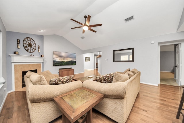 living area with visible vents, vaulted ceiling, a tile fireplace, light wood-style floors, and a ceiling fan