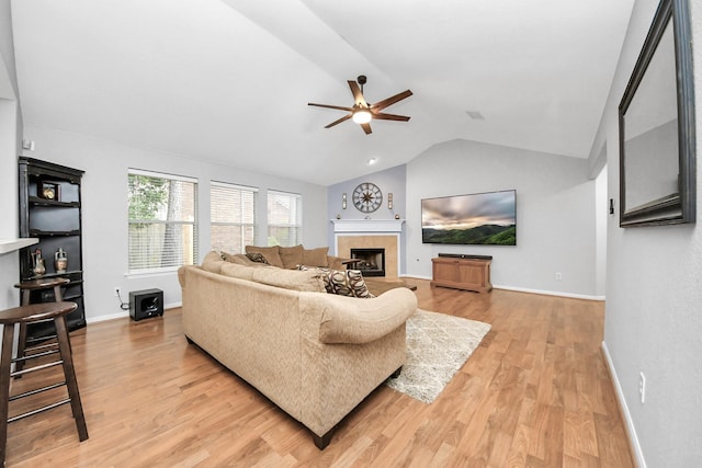 living room featuring light wood-style flooring, baseboards, a fireplace, lofted ceiling, and ceiling fan