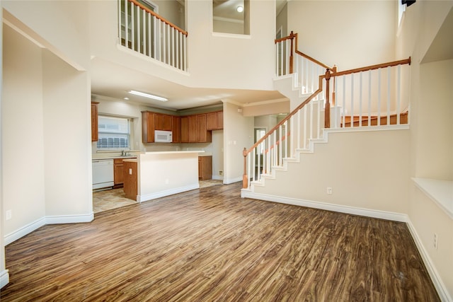 unfurnished living room with wood finished floors, baseboards, a high ceiling, a sink, and stairs