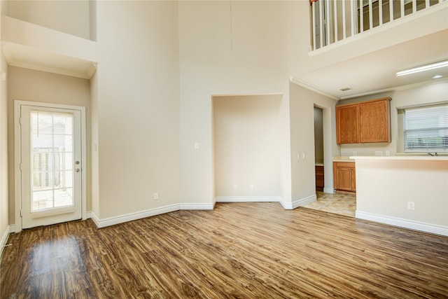 unfurnished living room featuring a wealth of natural light, wood finished floors, a towering ceiling, and ornamental molding