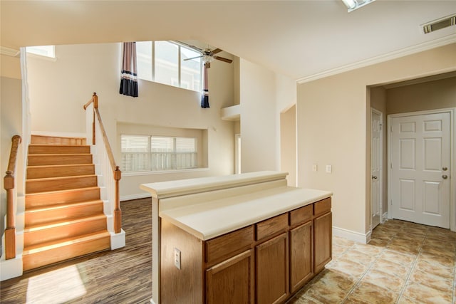 kitchen with a ceiling fan, brown cabinetry, visible vents, a kitchen island, and baseboards