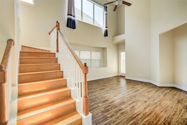 staircase featuring wood finished floors, baseboards, and a towering ceiling