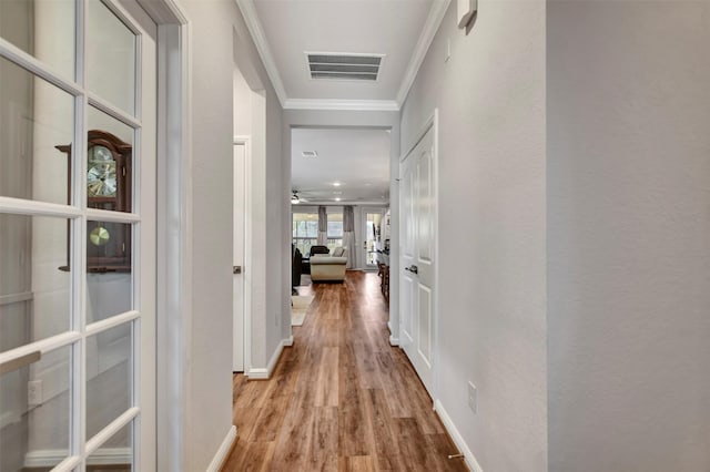 corridor with visible vents, baseboards, wood finished floors, and crown molding