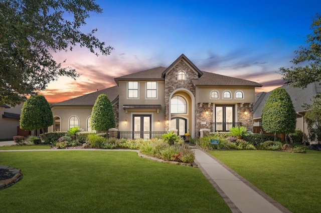 view of front of house with stone siding, stucco siding, french doors, and a lawn