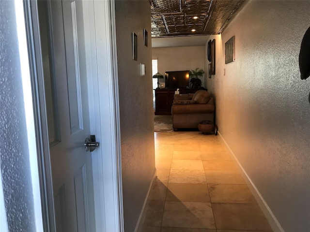 hall with tile patterned floors, an ornate ceiling, baseboards, and a textured wall