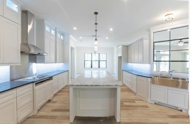 kitchen featuring a sink, glass insert cabinets, light wood-style floors, wall chimney exhaust hood, and backsplash