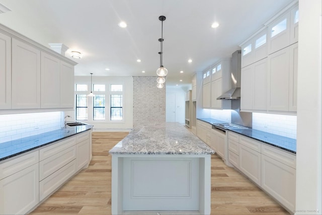 kitchen featuring a sink, tasteful backsplash, wall chimney exhaust hood, and a center island