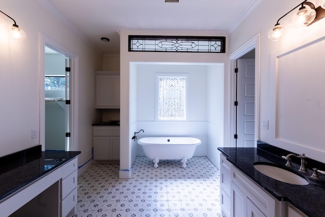 full bathroom featuring a soaking tub, two vanities, ornamental molding, a sink, and a wealth of natural light