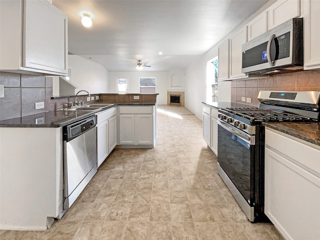 kitchen with a sink, stainless steel appliances, white cabinets, and a tiled fireplace