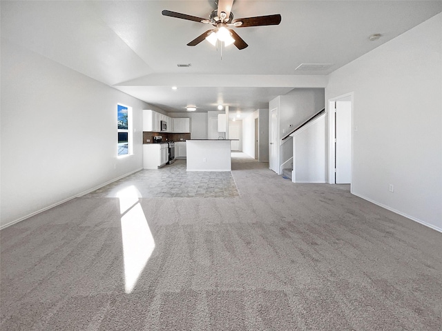 unfurnished living room with visible vents, light carpet, a ceiling fan, stairs, and vaulted ceiling